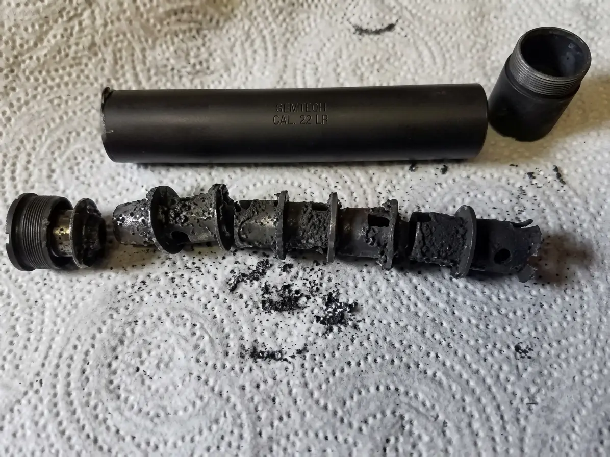 Disassembled rimfire suppressor showing heavy carbon and lead fouling on baffles